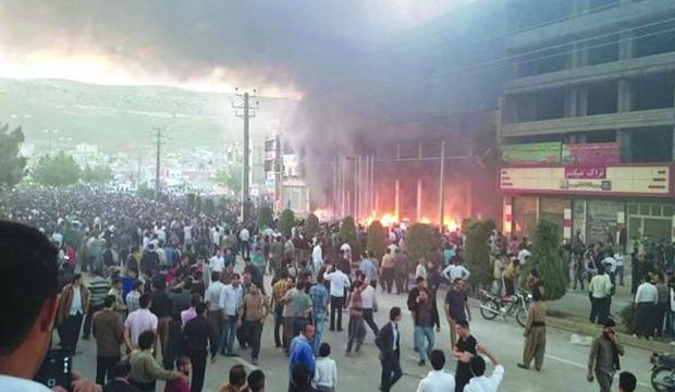 Protesters march as a building burns in the Iranian city of Mahabad, 421 miles (678 kilometers) northwest of Tehran, following the death of a young Kurdish woman who was sexually assaulted by an Iranian man, believed to be an Iranian intelligence operative, which led to her death. (Photo courtesy of Rudaw)