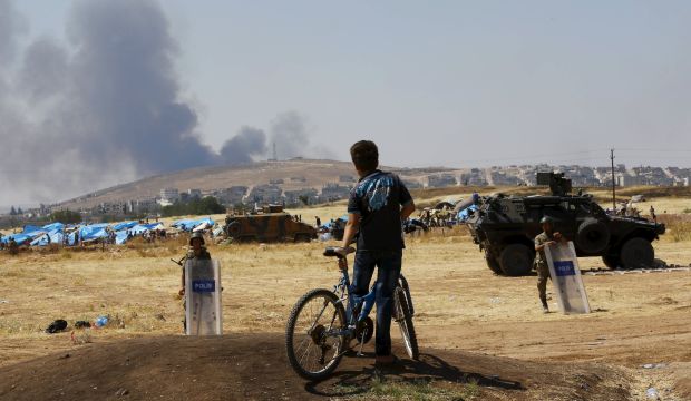 A Turkish Kurdish boy stands near the Mursitpinar border gate in Suruc in Sanliurfa province, Turkey, as smoke rises in the Syrian town of Kobani in the background on June 27, 2015. (REUTERS/Murad Sezer)