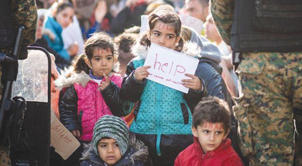 An Iranian child holding a message requesting help in a queue of Iranian refugees at the border between Greece and Macedonia (Getty)