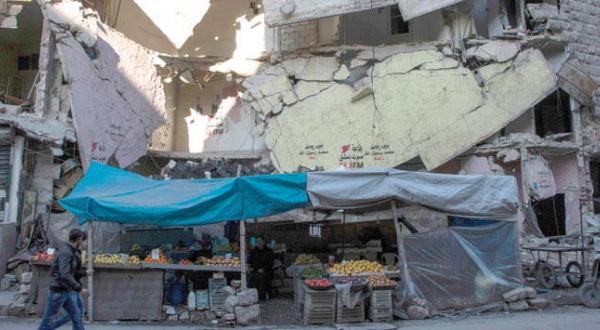 A young resident of the city of Aleppo, which is being bombed daily by the Russian air force, passes by a vegetable market and buildings that have been destroyed (AFP) 