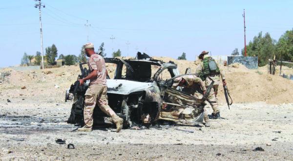 Iraqi security men inspect a burnt car in Hit after fierce clashes with ISIS, A.F.P