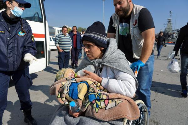 A woman giving the bottle to her baby, waits along with other migrants and refugees to board buses taking them to the registration hotspot of Moria, from the port of Mytilene on the Greek island of Lesbos on March 29, 2016, after being rescued by Frontex and Greek coast guards. / AFP PHOTO
